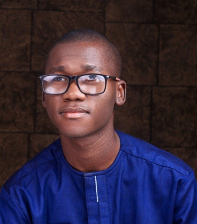 Portrait of DivineGift David Usman, visually impaired CEO of ZATS, wearing glasses and a blue shirt, smiling at the camera.